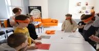 Dzieci przy stole z zawiązanymi oczami wcielają się w role osób niewidomych.