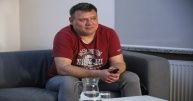Borys Tynka w czerwonej koszulce siedzi na kanapie.