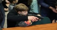 Chłopiec z pomocą osoby dorosłej trzyma broń.